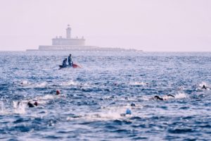 unrecognizable men on powerboat on wavy sea near swimming athletes